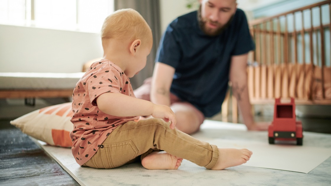 Pappa och ett litet barn leker med en bil på golvet.