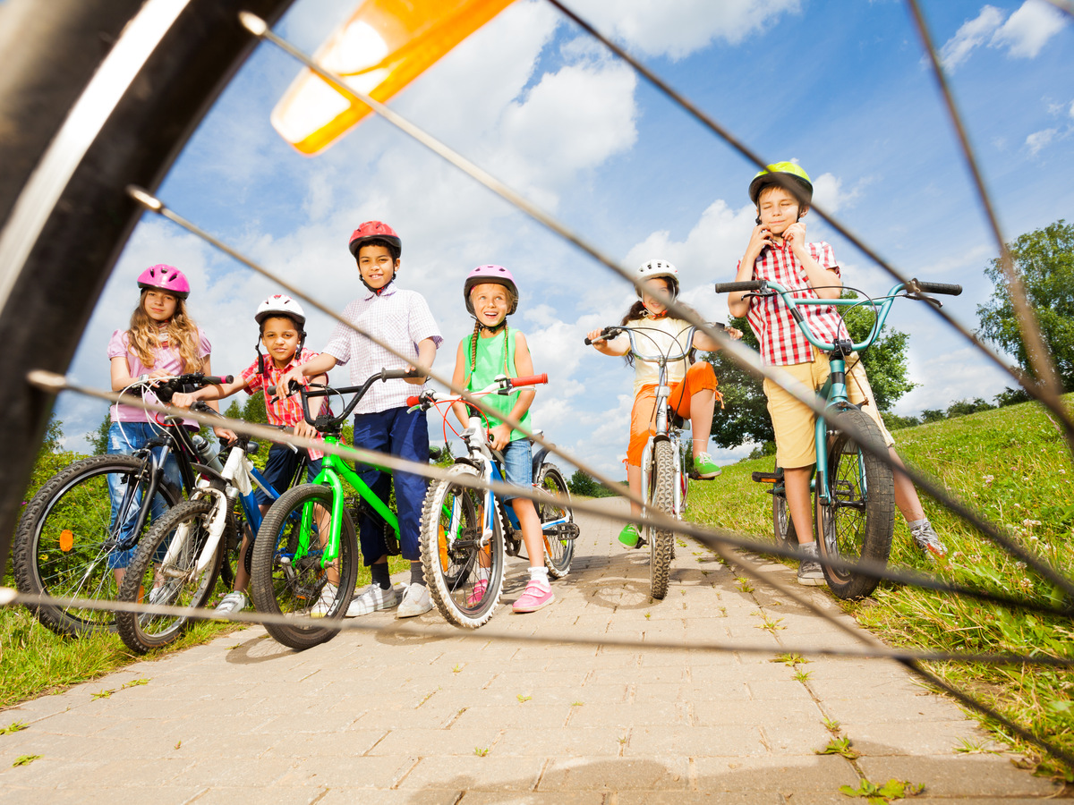 View from bicycle spoke on kids with helmets and bikes on path in field