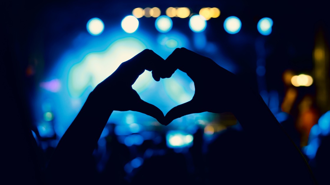 Händer formar ett hjärta framför en scen.