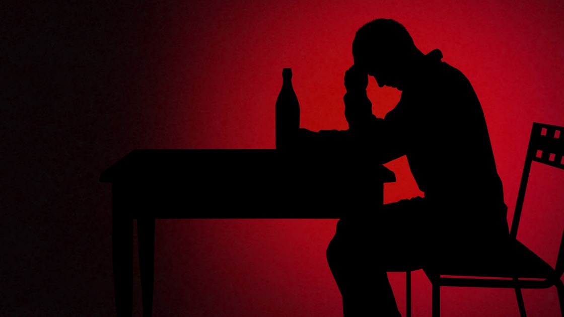 Alkoholiserad man i silhuett vid ett bord.