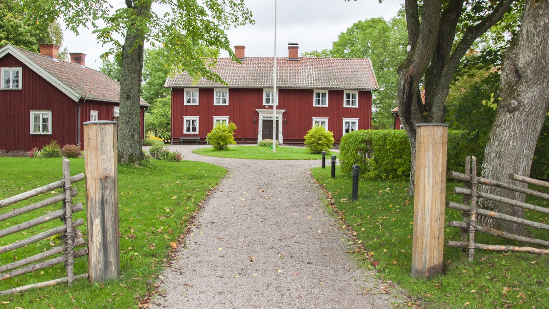 Hembygdsgård Balteryd. Bild tagen en bit ifrån, men större rött trähus i mitten. Två mindre byggnader på vardera sida huvudbyggnaden. Närmast i bild gärdsgård.
