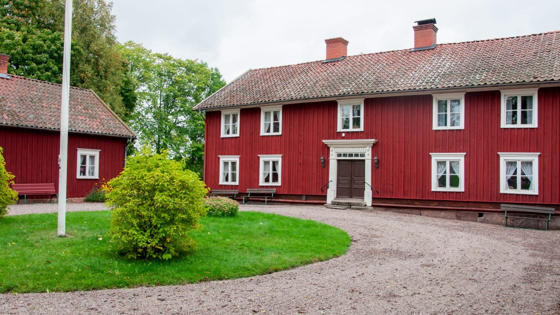 Balteryds hembygdsgård. På bilden syns två röda byggnader med vita fönsterfoder, grusplan samt gräsrondell med buskar.