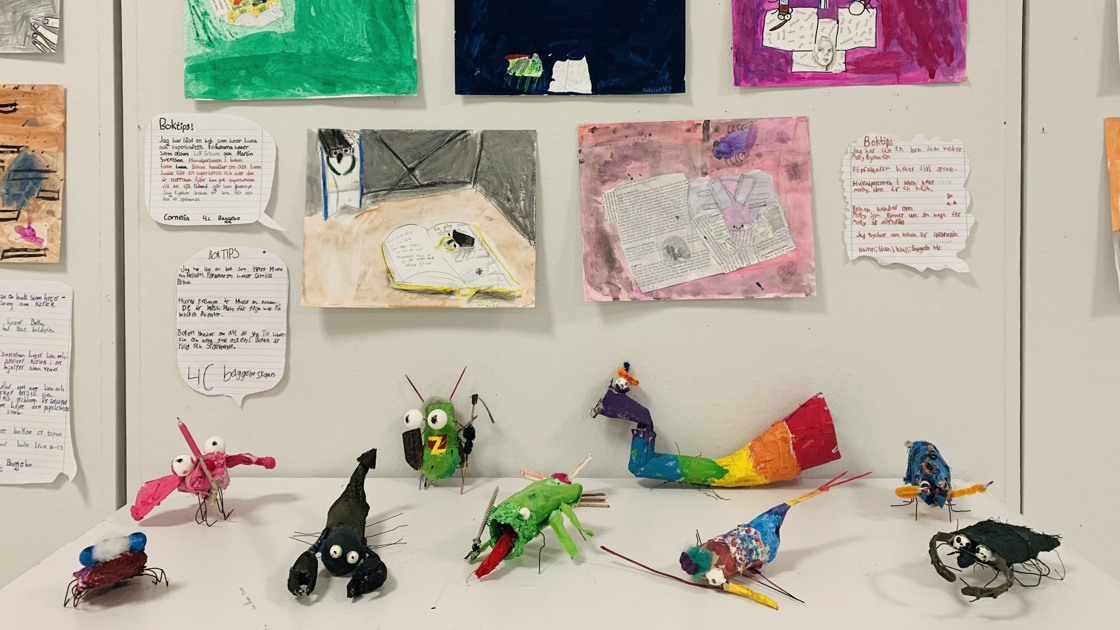 Nertill i bild är ett bord med flera figurer som föreställer fantasiinsekter. Ovanför hänger teckningar.