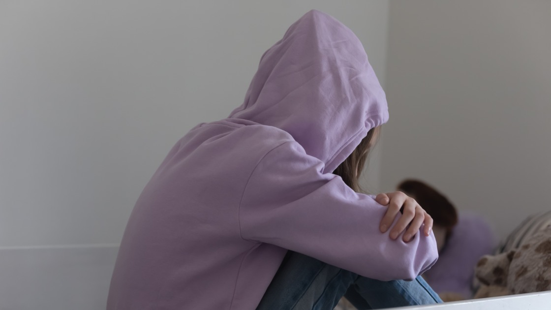 Ledsen tonåring som sitter uppkrupen i en säng.