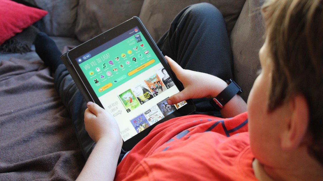 Ett barn sitter i en soffa, hållandes en  Ipad med appen Bibblix.