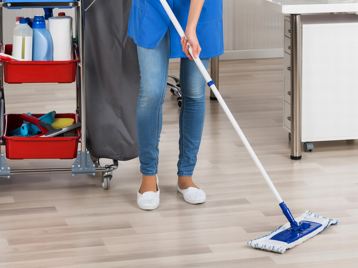 Full length portrait of happy female janitor mopping floor in office
