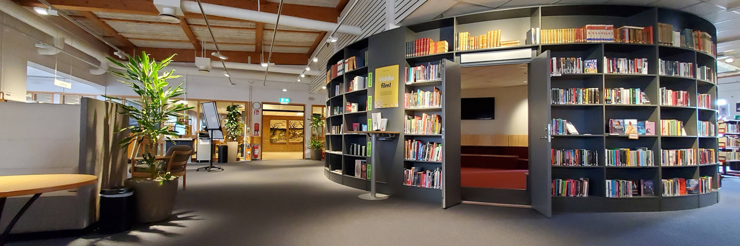 Miljöbild inifrån Tibro bibliotek. Stort öppet rum med mörk matta. Till höger i bild rotunda med bokhyllor och böcker.