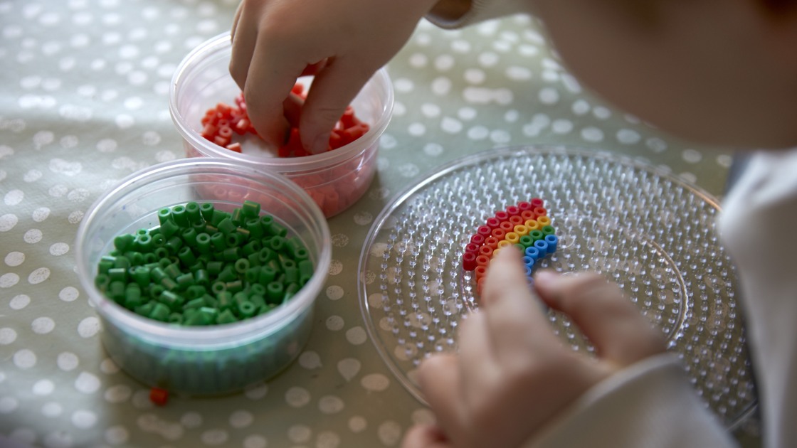 Ett barn pärlar en regnbåge på en pärlplatta.