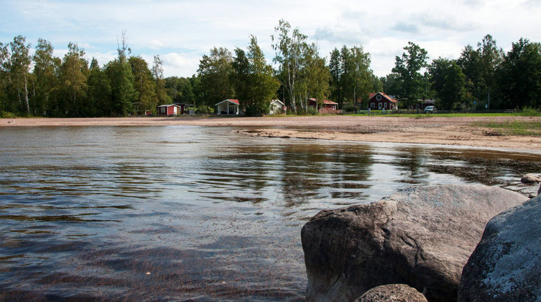 Fagersannabadet. Fotot är taget från en stor sten i vattnet och bakgrunden syns strandkant, träd och några stugor.