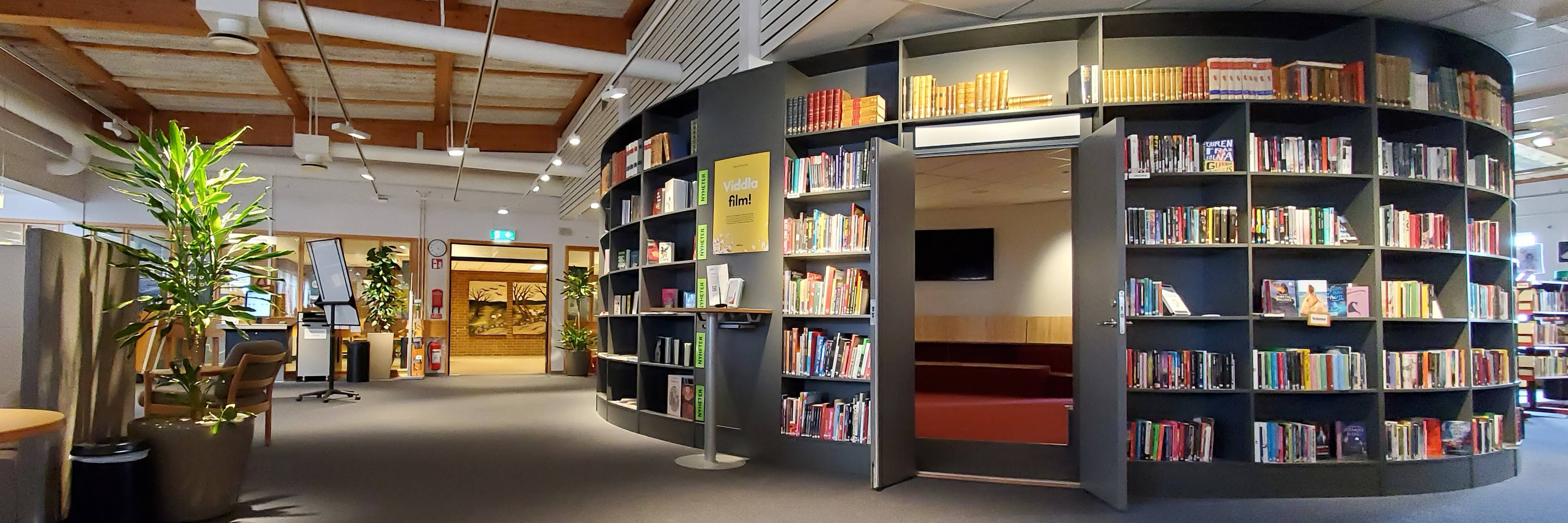 Miljöbild inifrån Tibro bibliotek. Stort öppet rum med mörk matta. Till höger i bild rotunda med bokhyllor och böcker.