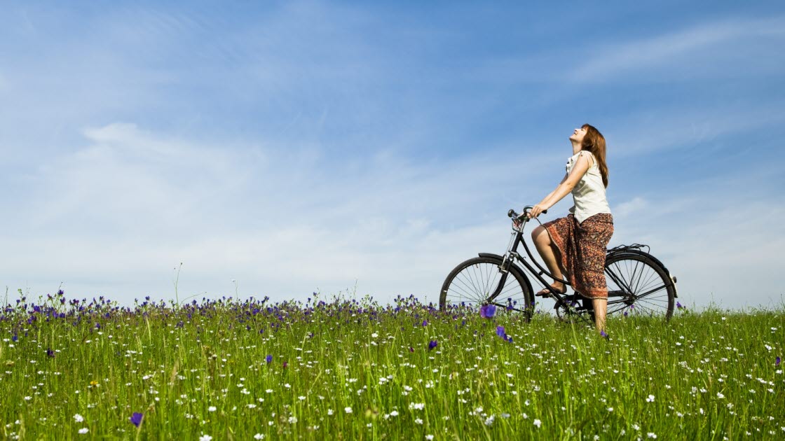 Ung kvinna med cykel på en grön äng. 