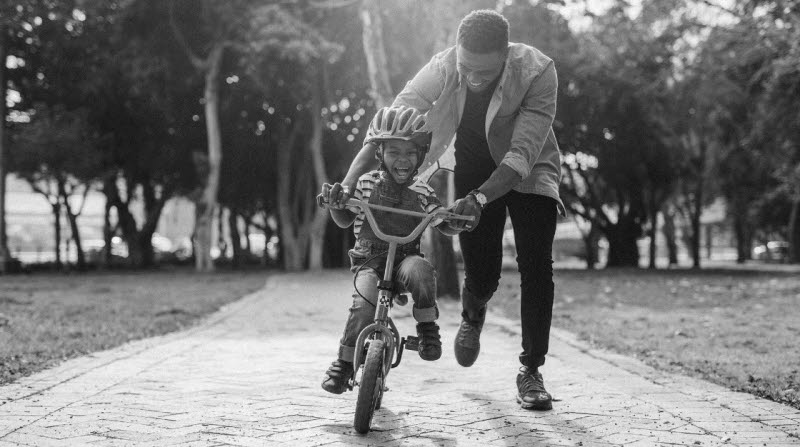 Pappa som stöttar sin son som lär sig cykla